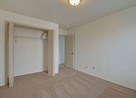 A spacious bedroom here at St. James Place with soft beige carpet, cream walls, and a large closet with sliding doors. A simple layout and neutral tones create a clean and inviting atmosphere.