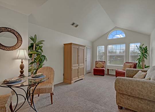 A spacious living room here at St. James Place with soft beige carpet, high vaulted ceilings, and large windows that bring in natural light. A cozy seating area and open layout create a bright and inviting atmosphere.