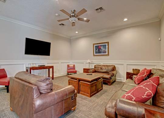 A comfortable resident lounge here at St. James Place with plush seating, warm lighting, and a large wall-mounted TV. A spacious layout and inviting atmosphere create a perfect space for relaxing or socializing.