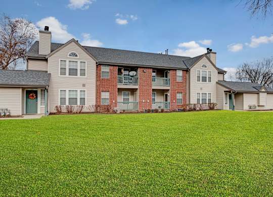 A charming exterior here at St. James Place with classic brick and siding, private balconies, and large windows. A spacious green lawn and well-maintained landscaping create a peaceful and welcoming community setting.