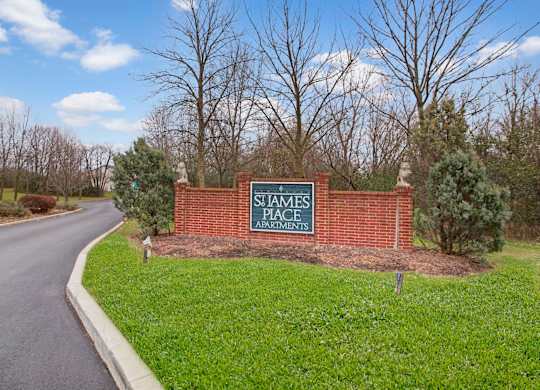 A welcoming community entrance here at St. James Place with a classic brick monument sign and landscaped greenery. A curved driveway and mature trees create a peaceful and inviting first impression.