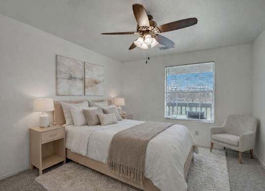 A bright bedroom here at St. James Place with soft beige carpet, cream walls, and a large window that brings in natural light. A ceiling fan and cozy layout create a comfortable and inviting atmosphere.