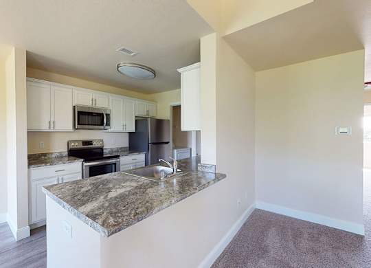 A modern kitchen here at St. James Place with white cabinets, granite-style countertops, and stainless steel appliances. A breakfast bar with a built-in sink opens to the living area, creating a bright and inviting open layout.