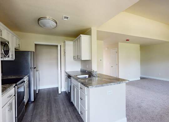 A spacious kitchen here at St. James Place with white cabinets, granite-style countertops, and stainless steel appliances. A breakfast bar overlooks the open living area, creating a bright and inviting layout.