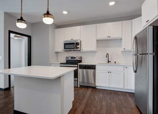 A modern kitchen here at The Lafayette featuring bright white cabinets, a large island, stainless steel appliances, subway tile backsplash, warm wood floors, and stylish pendant lighting above the island.