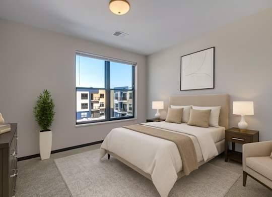 A peaceful bedroom here at The Lafayette featuring soft neutral bedding, matching nightstands with lamps, a light area rug, a cozy accent chair, and a large window bringing in bright, refreshing natural light.
