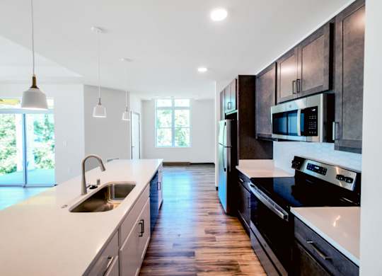 A modern kitchen here at Van Buren East with stainless steel appliances and dark wood cabinets. A long center island with sink and pendant lighting overlooks an open living area with access to a private balcony.