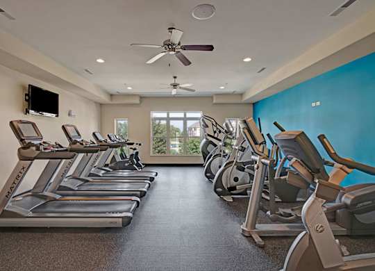A fitness center here at Van Buren Place featuring modern cardio equipment, a bold blue accent wall, and bright windows, creating an energizing, spacious, and motivating workout space.