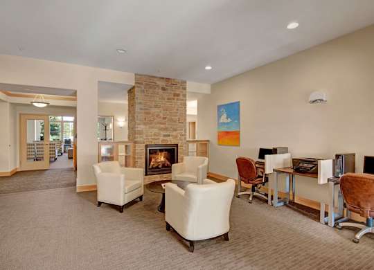A welcoming resident lounge here at Van Buren Place with comfortable seating arranged around a cozy stone fireplace. A business center with computers and desks provides convenience, while warm lighting and soft carpeting create a relaxed, inviting atmosphere.