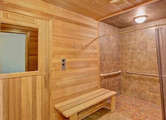 A relaxing sauna room here at Van Buren Place with warm wood-paneled walls, a built-in bench, and convenient hooks. A tiled shower area sits nearby, creating a comfortable, spa-like atmosphere for residents to unwind.