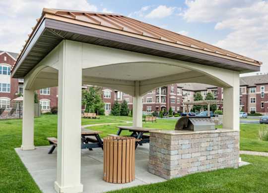 A covered outdoor grilling area here at Van Buren Place with a built-in barbecue and picnic table seating. A landscaped lawn and nearby apartment buildings create a welcoming, community-friendly atmosphere for outdoor gatherings.