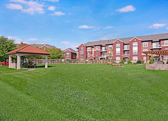 A spacious green courtyard here at Van Buren Place with open lawn space and shaded picnic areas. A pergola grilling station and nearby apartment buildings create a peaceful, park-like atmosphere for residents.
