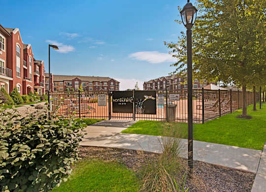 A gated pool entrance here at Van Buren Place with secure fencing and landscaped surroundings. A nearby sidewalk, green lawn, and charming lamp post create a clean, welcoming community atmosphere.