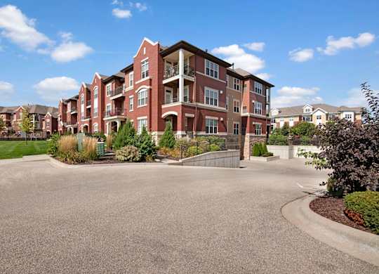 A beautiful apartment building exterior here at Van Buren Place with private balconies and attractive brick architecture. A landscaped entrance, green lawn, and nearby parking area create a clean, upscale community setting.