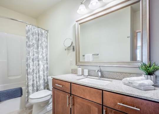 A bathroom here at Van Buren Place featuring a spacious vanity with warm wood cabinetry, large mirror, and a shower-tub combo that makes the space feel clean, bright, and comfortable.