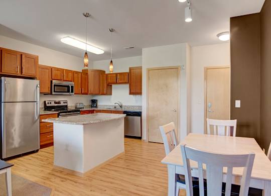 A dining area here at Van Buren Place featuring a light wood table and matching chairs beside a bright, open kitchen with warm cabinets and an inviting, comfortable layout.