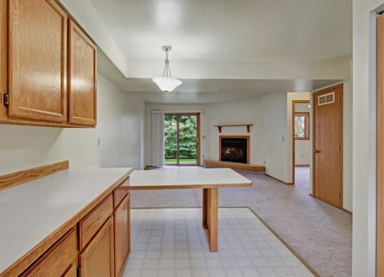 Spacious, bright interior here at Wildwood Estates Apartments with light wood cabinets, tiled floors transitioning to carpet. Features fireplace, sliding door to greenery, modern yet cozy feel.