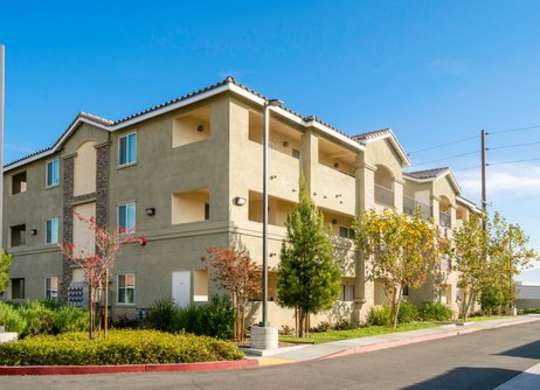A row of beige apartment buildings with trees in front.