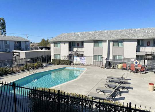 A pool surrounded by a black fence and chairs.