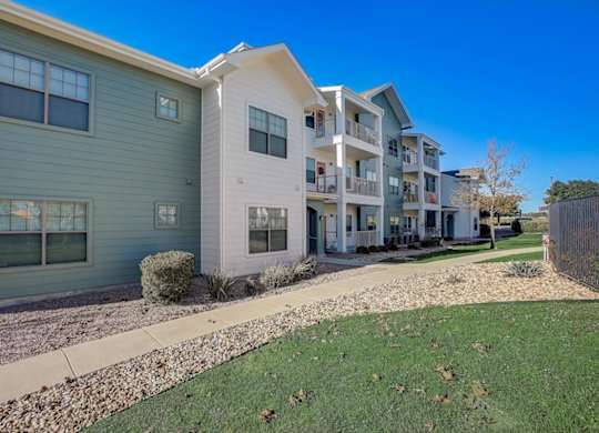Apartment buildings with sidewalks, rock landscaping, and green lawn.