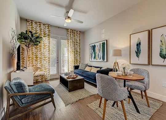 A living room with a blue couch, a wooden chair, a wooden table, and a ceiling fan.