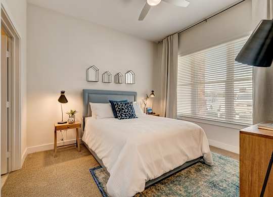 A bedroom with a bed, a nightstand, and a window with blinds.