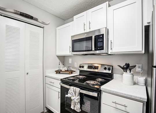 A white kitchen with a black stove top oven and a microwave above it.