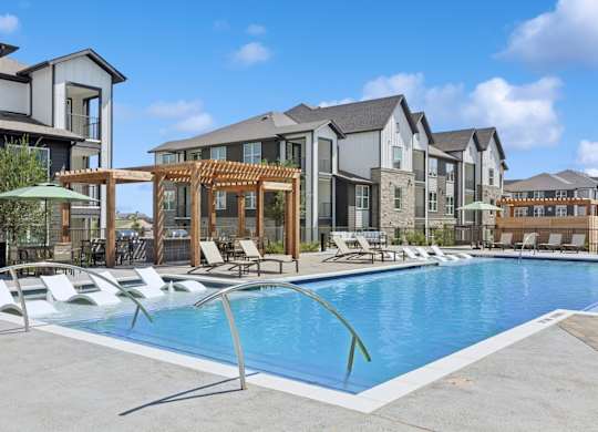 A swimming pool surrounded by lounge chairs and umbrellas in front of apartment buildings.