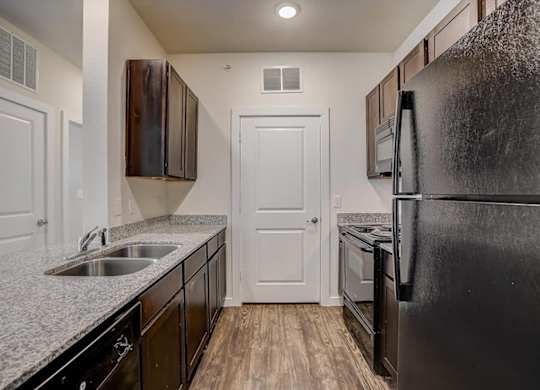 Galley kitchen with granite countertops, double sink, and black appliances.