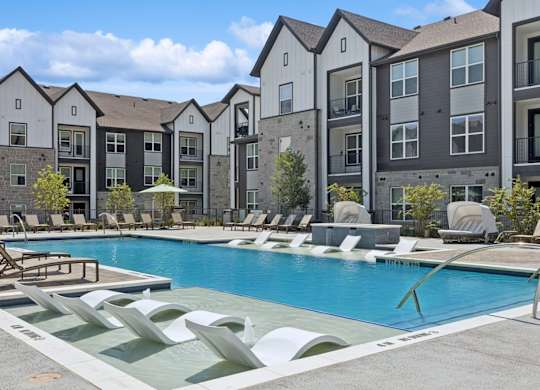 A pool surrounded by lounge chairs and buildings in the background.