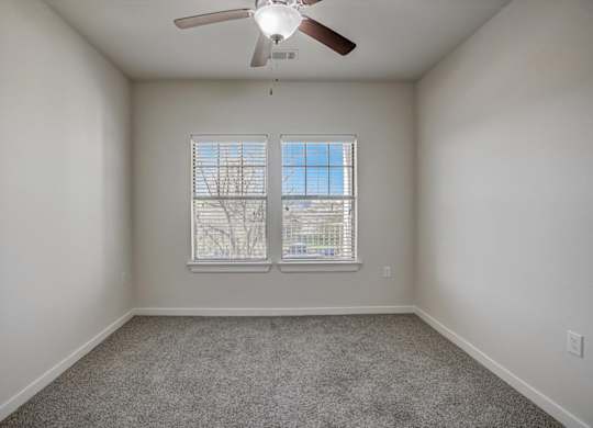 Secondary bedroom with twin windows, ceiling fan, and soft carpeting.