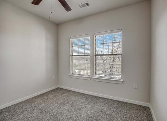Carpeted bedroom with two windows, white blinds, and ceiling fan.