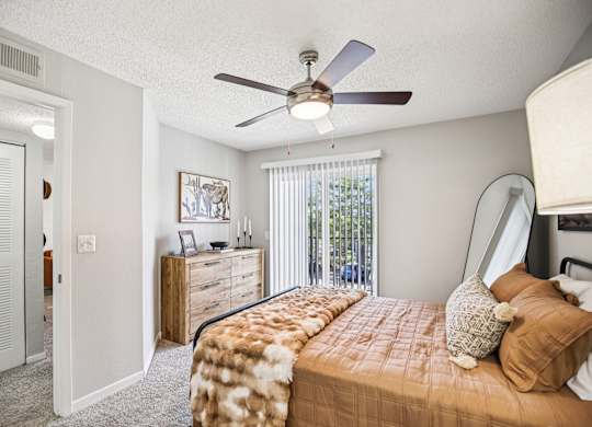 A bedroom with a bed, dresser, and a ceiling fan.