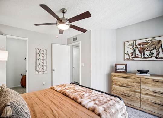 A bedroom with a bed, a ceiling fan, and a dresser.