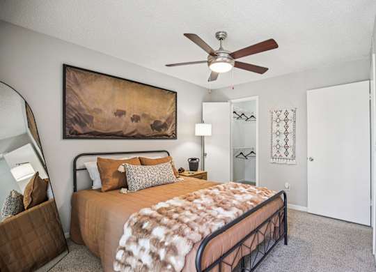 A bedroom with a bed, a ceiling fan, and a painting on the wall.