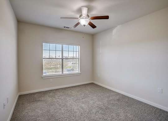 Bright bedroom with large window, ceiling fan, and neutral walls.