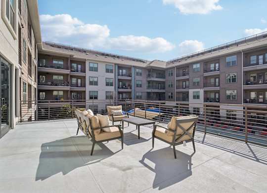 A patio with chairs and a table is in front of apartment buildings.