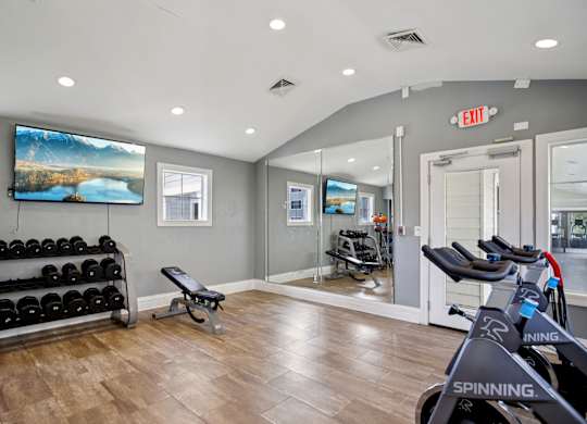 A gym with a row of spinning bikes and a bench with weights.