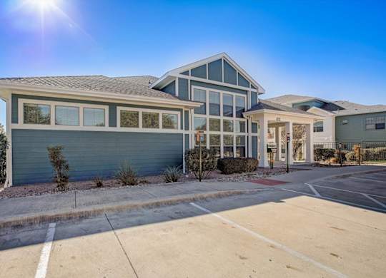 Clubhouse exterior with large windows, blue siding, and landscaped frontage.