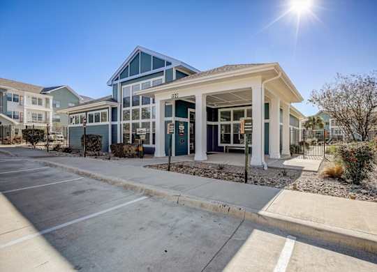 Covered clubhouse entrance with columns, glass doors, and xeriscape beds.
