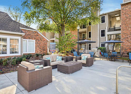 A patio with a couch, chairs, and a table with a tree in the background.