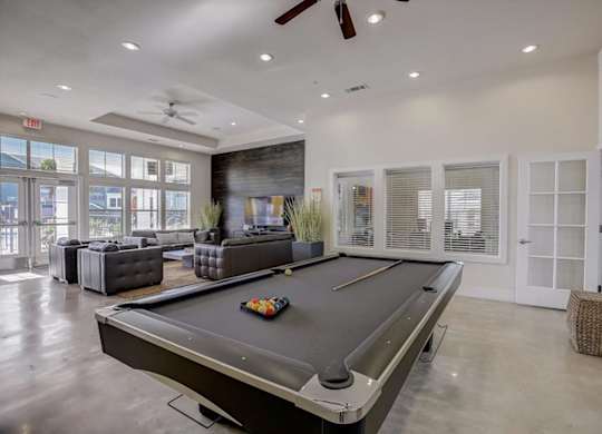 Pool table in clubhouse with lounge seating and oversized windows nearby.