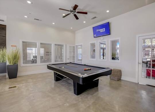 Indoor game room with pool table, wall-mounted TV, and polished concrete floors.