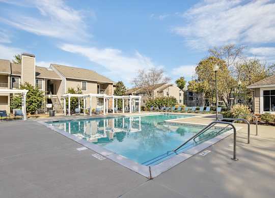 A swimming pool surrounded by a concrete floor and metal railings with a building in the background.