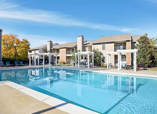 A large swimming pool in front of a building with a white pergola.