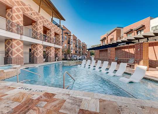 A swimming pool surrounded by white lounge chairs and a brick building.