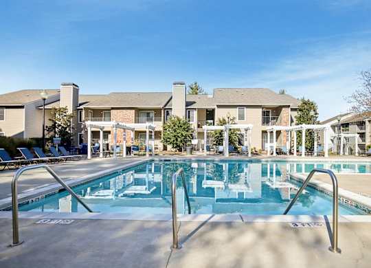 A large swimming pool in front of a building with lounge chairs around it.
