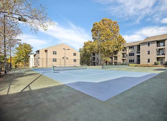 A tennis court is surrounded by apartment buildings.