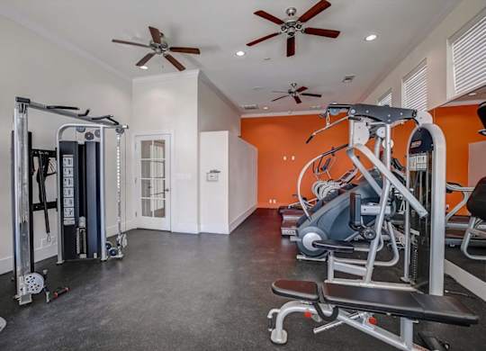 Fitness center with strength machines, treadmills, and orange accent wall.