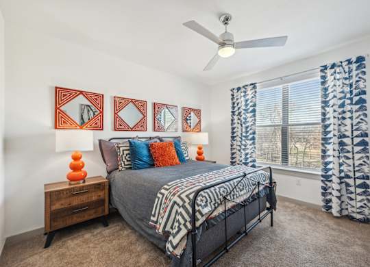 A bedroom with a bed, a ceiling fan, and a window with curtains.